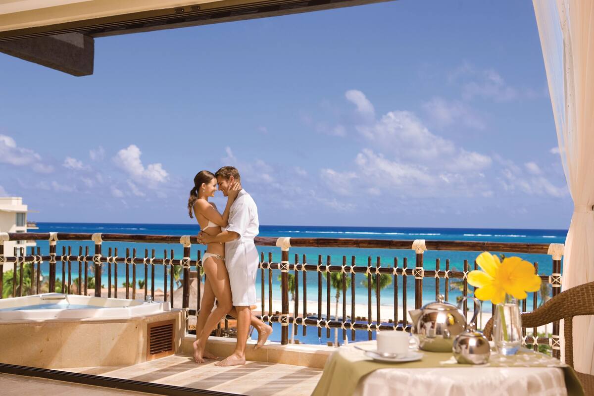 A couple embracing on a balcony overlooking a beach with a clear sky.