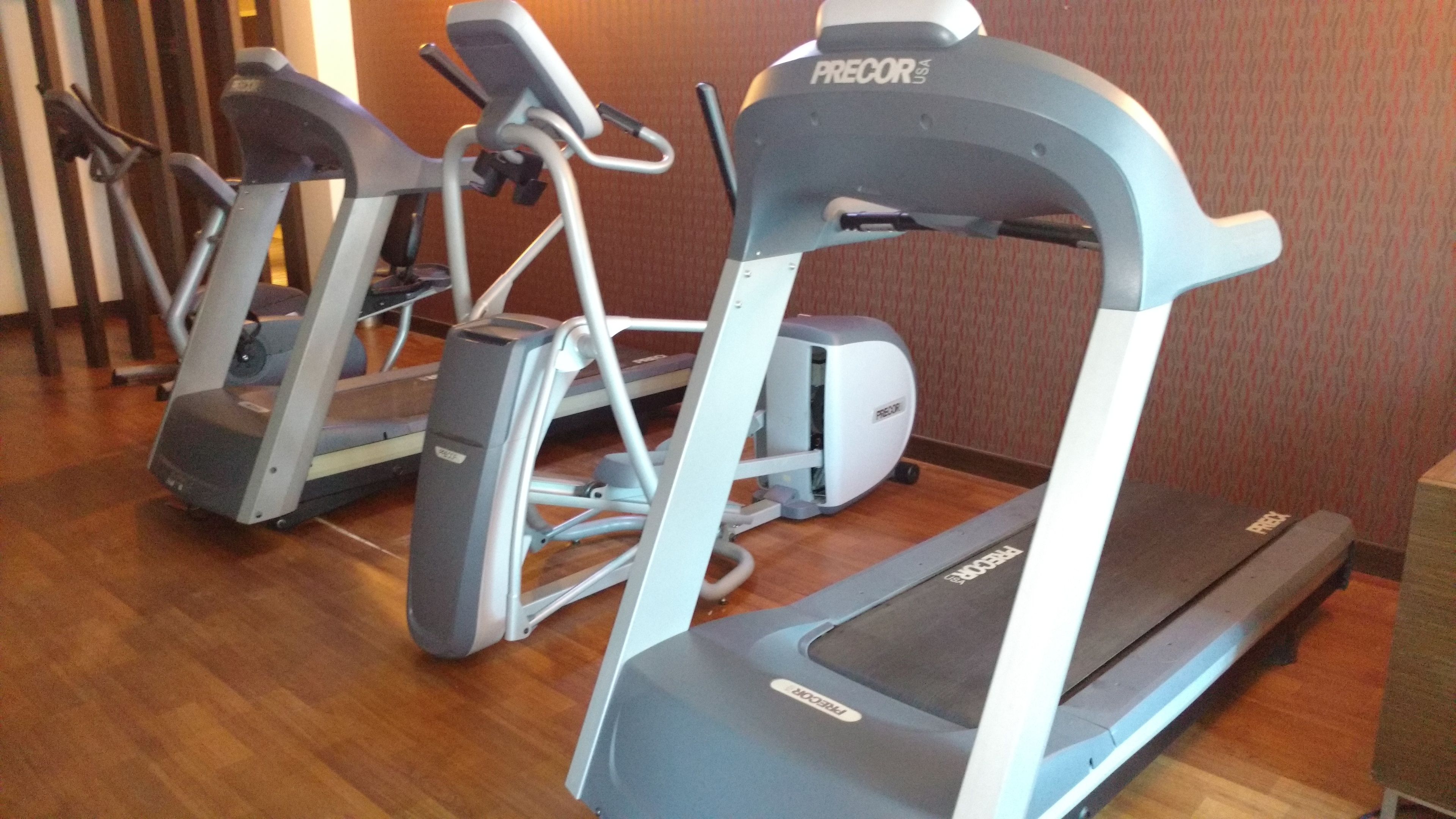 A row of treadmills in a room with wooden flooring and patterned walls.