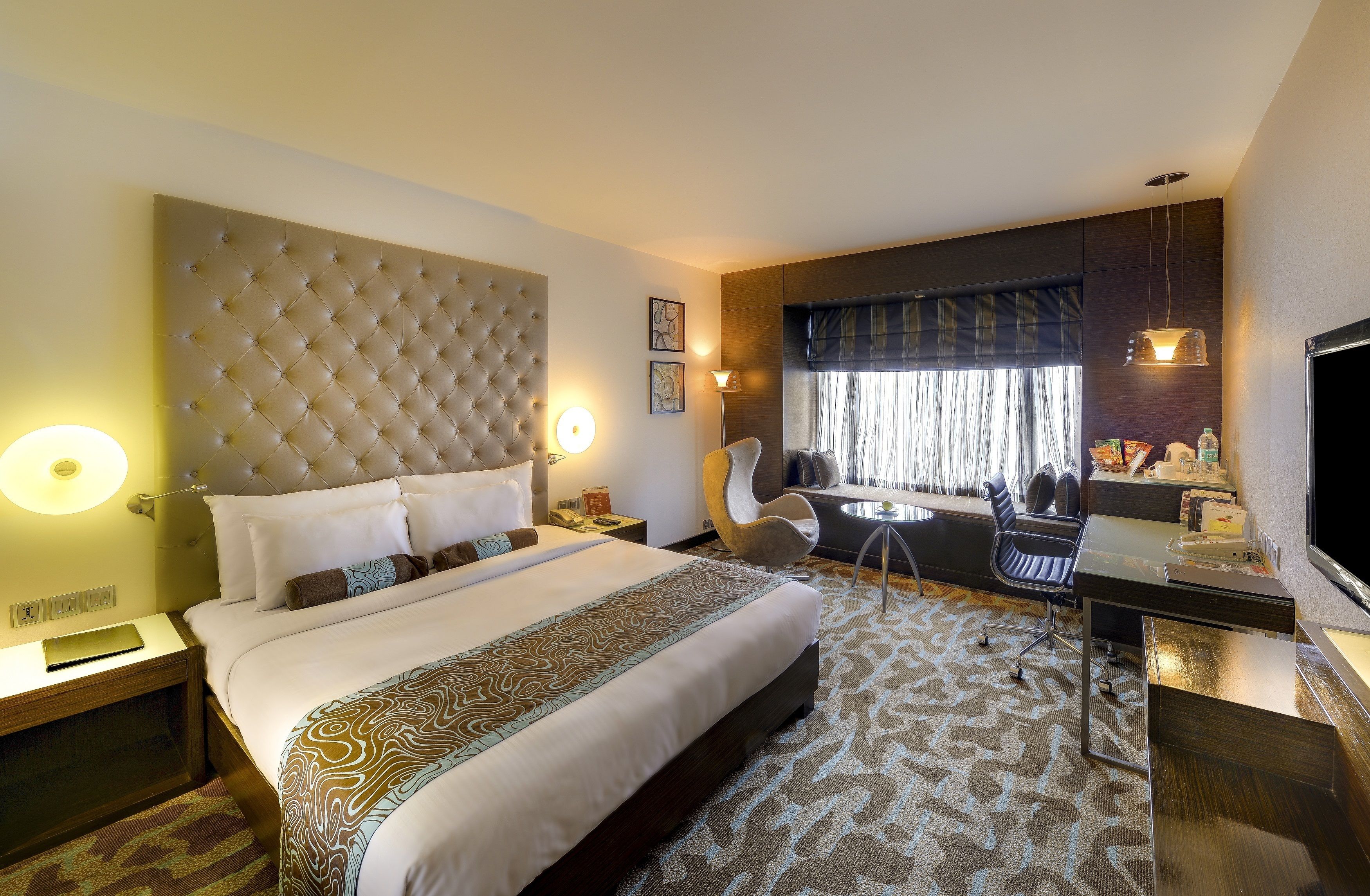 A hotel room with a large bed, a desk, a chair, and a TV.