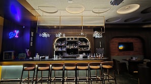 Zona de bar con un letrero de neón, estantes llenos de botellas de licores y una pared de ladrillo.