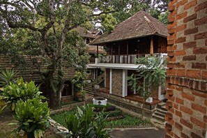 A traditional building with a balcony, surrounded by lush greenery and a well-maintained garden. - Hotel Ambadi (Peermade)