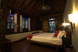 Quarto de madeira com cama, um banco e janela com cortinas.