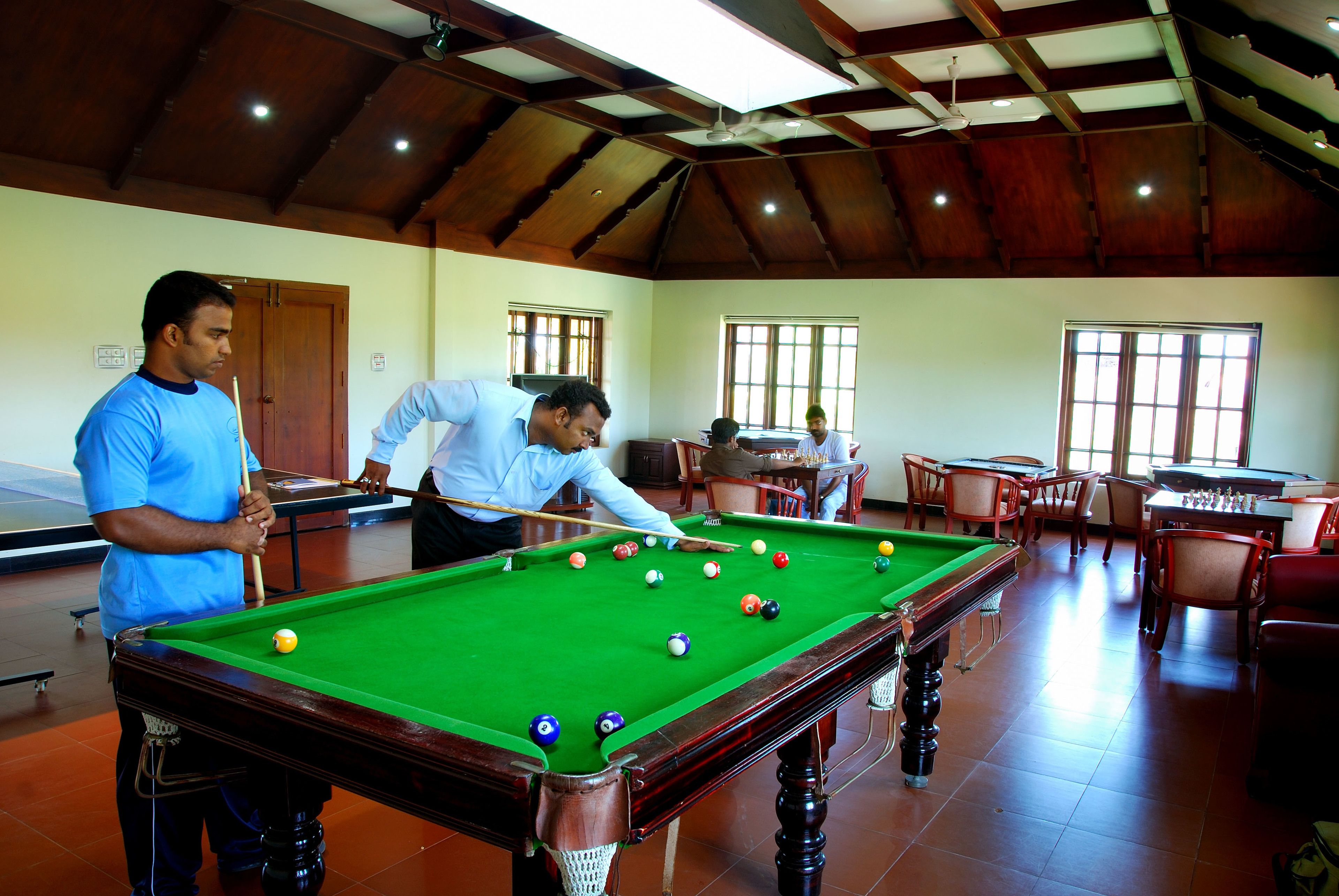 A pool table in a room with wooden ceiling beams, chairs, and a table with a foosball table.