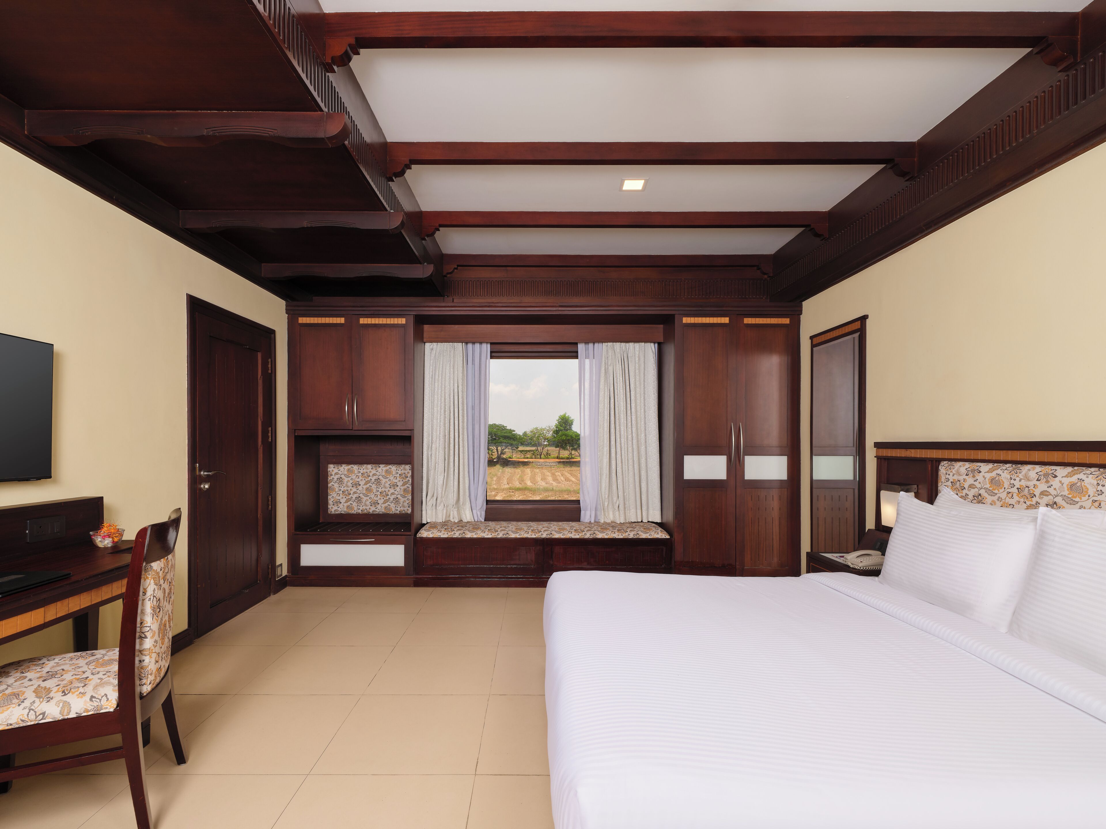 Habitación de hotel con una cama grande, un escritorio con silla, televisión y ventana con cortinas.