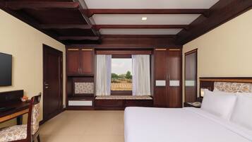 A hotel room with a large bed, a desk with a chair, a TV, and a window with curtains.