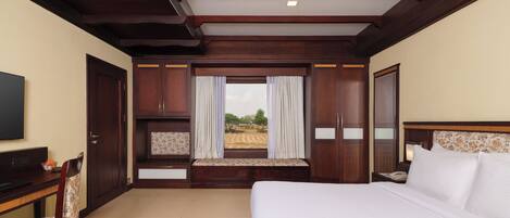 Habitación de hotel con una cama grande, un escritorio con silla, televisión y ventana con cortinas.