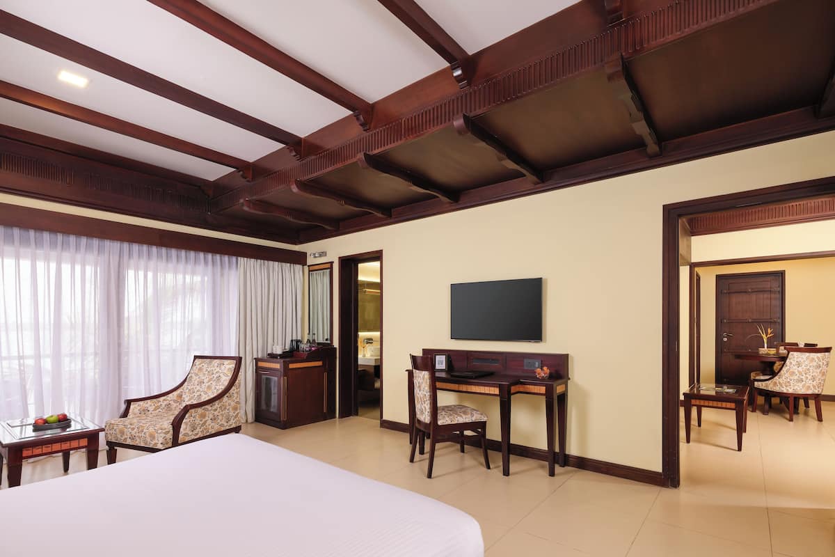 Ein Hotelzimmer mit einem großen Bett, einem Schreibtisch, zwei Stühlen, einem Fernseher und einer Tür zu einem weiteren Raum.