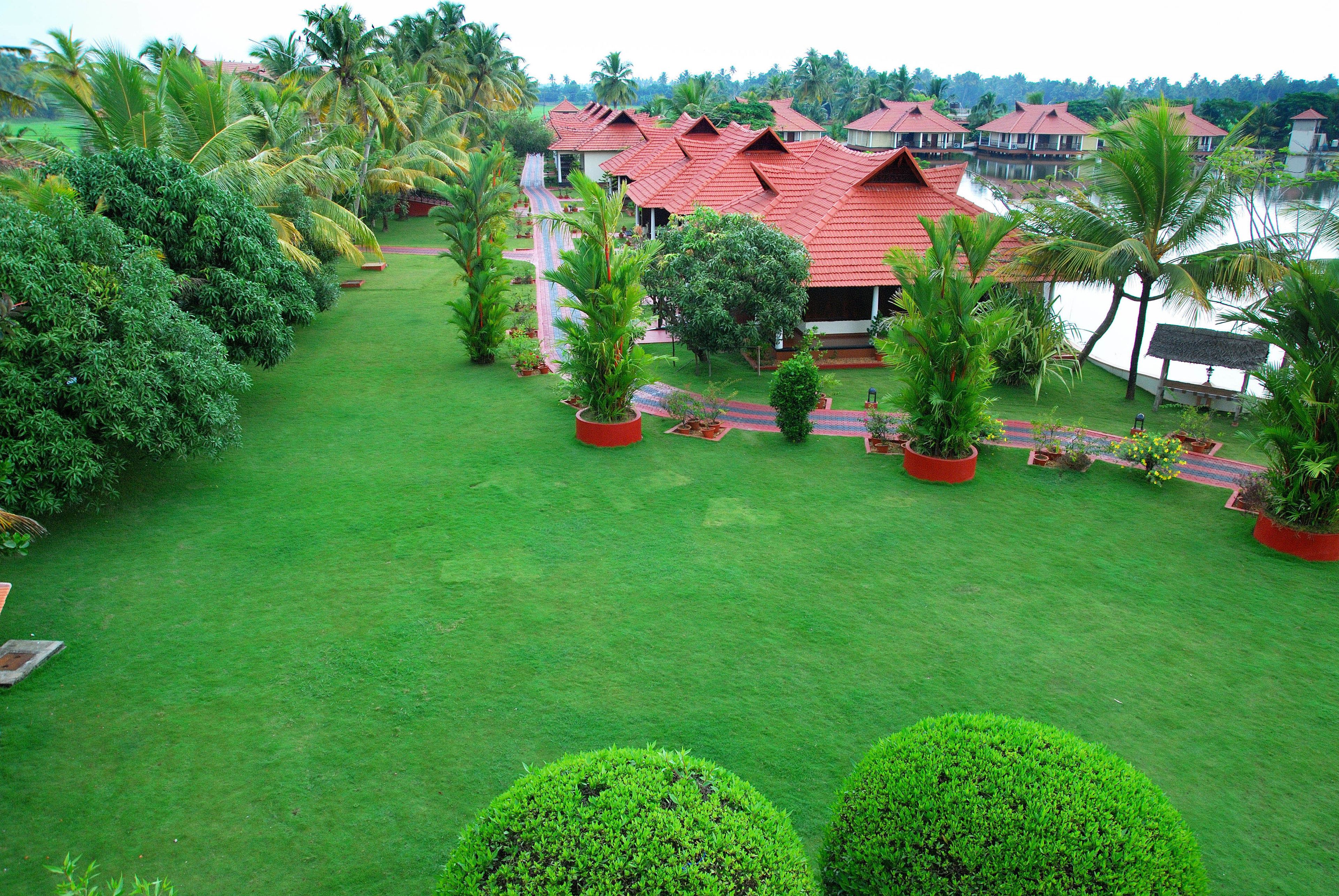 A resort with red-roofed buildings, lush green lawns, and palm trees.