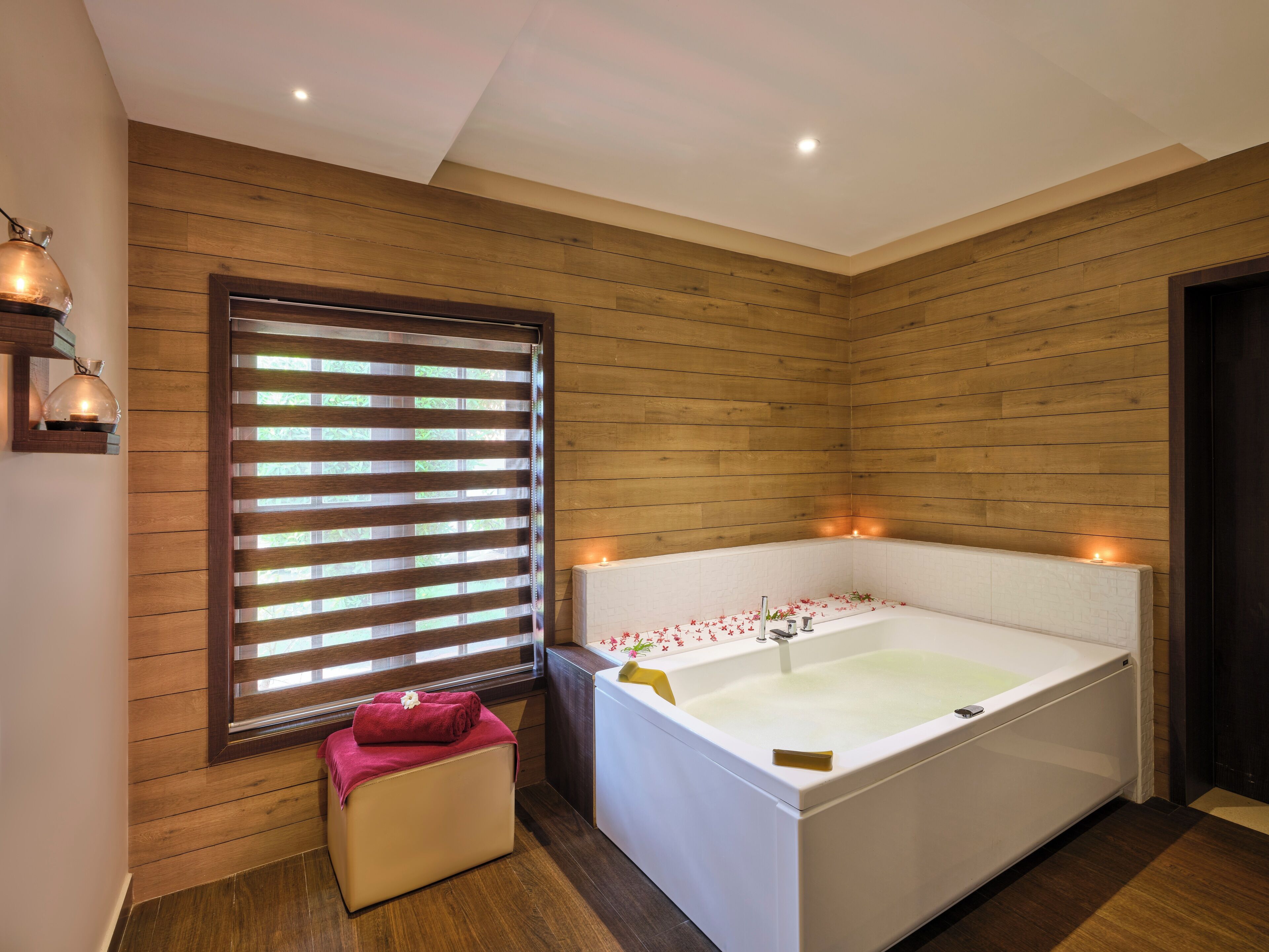 A modern bathroom with a large bathtub, wooden paneling, and a window with blinds.