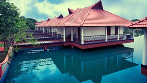A traditional house with a red tiled roof, a balcony with a metal railing, and a reflection in the water. - Sterling Lake Palace Alleppey (Ambalapuzha)