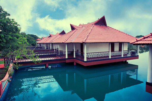 A traditional house with a red tiled roof, a balcony with a metal railing, and a reflection in the water. - Sterling Lake Palace Alleppey (Ambalapuzha)