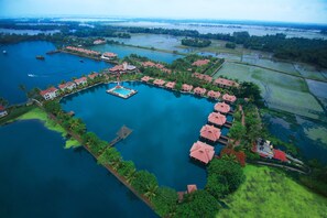 Vista aérea de um resort com piscina central, ligada por passarelas, cercado por vegetação exuberante e lagoas.