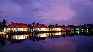 A row of overwater bungalows with red roofs, reflecting on the water, surrounded by palm trees. - Sterling Lake Palace Alleppey (Ambalapuzha)