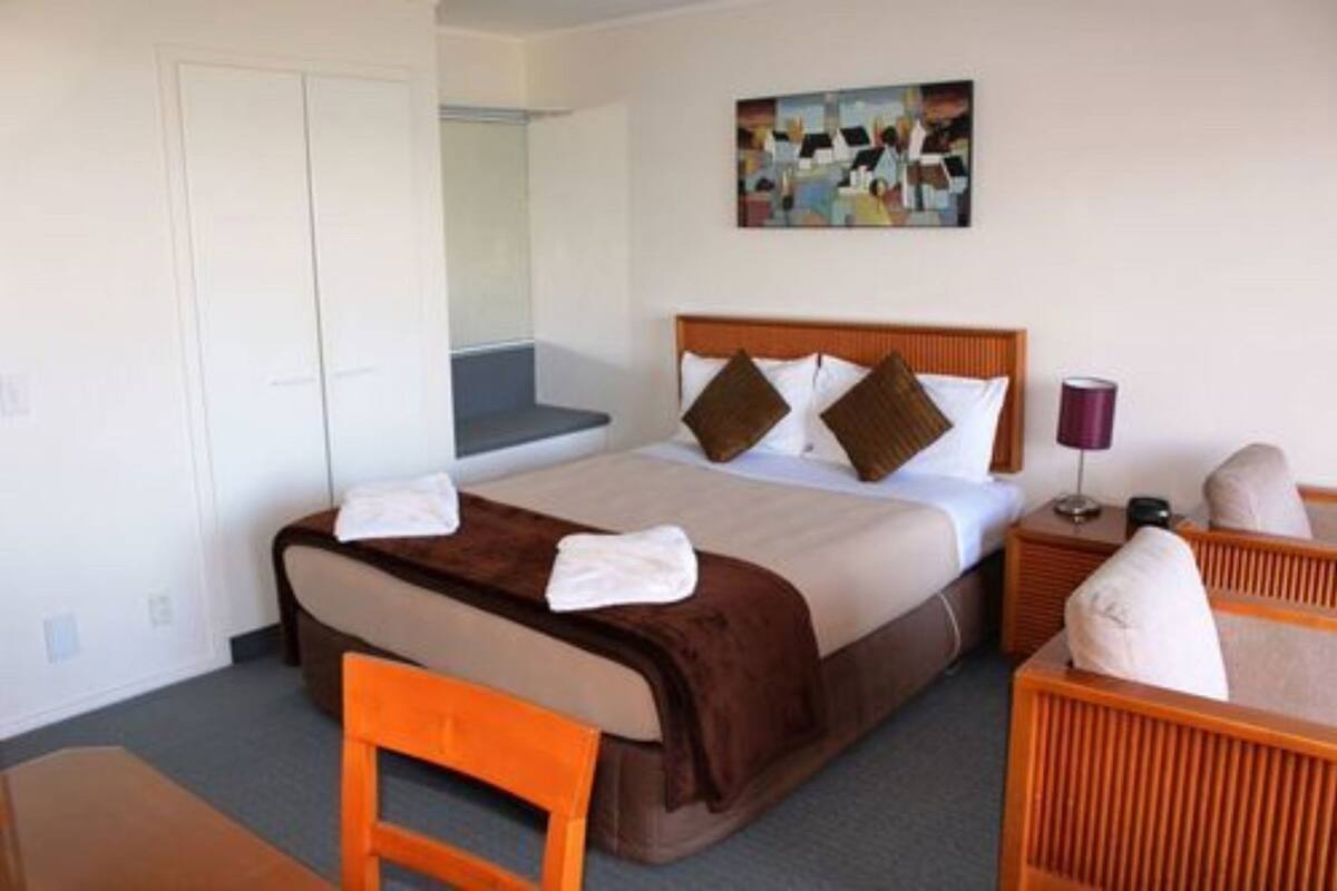 A hotel room with a bed, a chair, a bedside table, a lamp, and a painting on the wall.