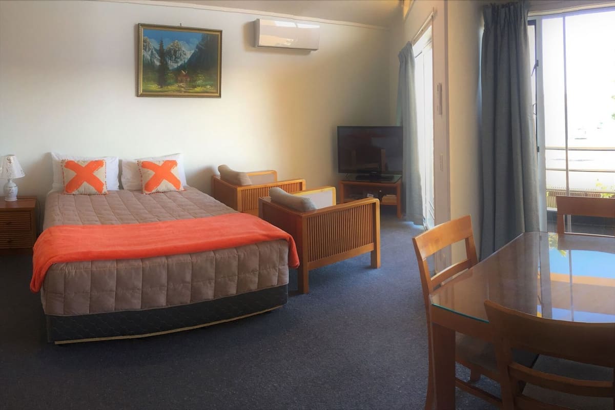 A hotel room with a bed, a television, a dining table, and a painting on the wall.