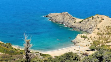 Un paisaje costero con un promontorio rocoso, mar azul cristalino y una playa arenosa con sombrillas.