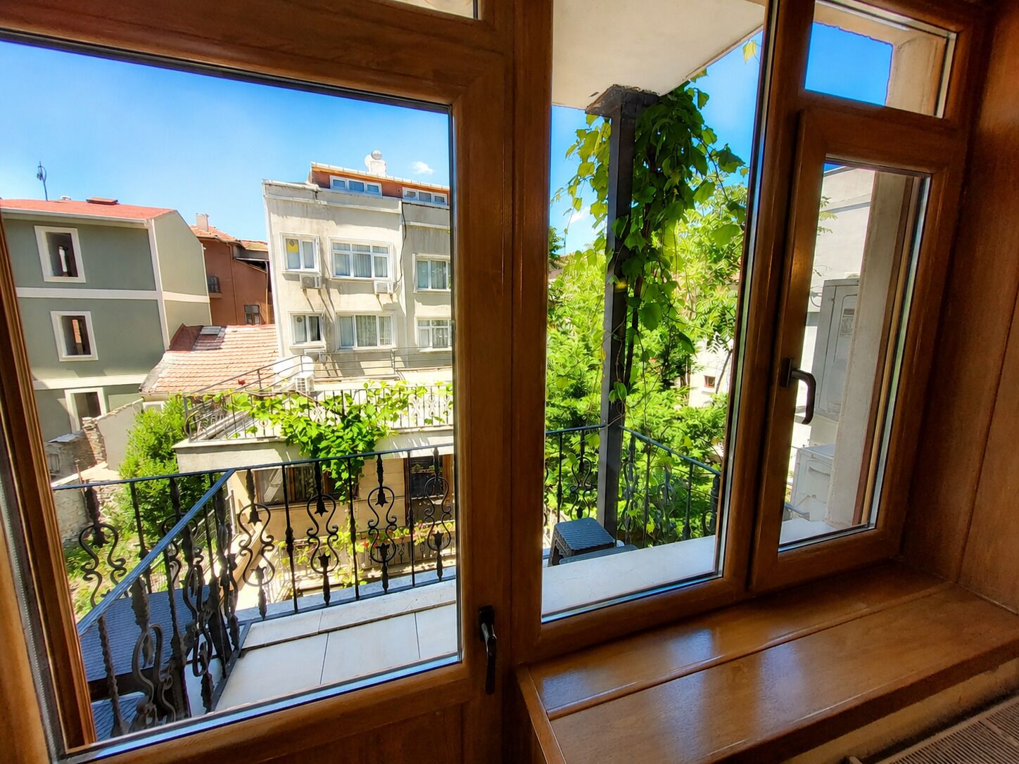 Blick aus einem Fenster mit Balkon auf ein Wohngebiet mit Gebäuden und Grünflächen.