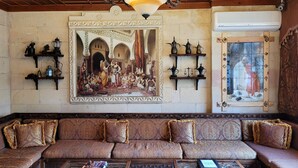 Une pièce comprenant un grand canapé, deux tables basses, un lustre et un mur orné d’un grand tableau et de plusieurs étagères sur lesquelles sont disposés des objets décoratifs.