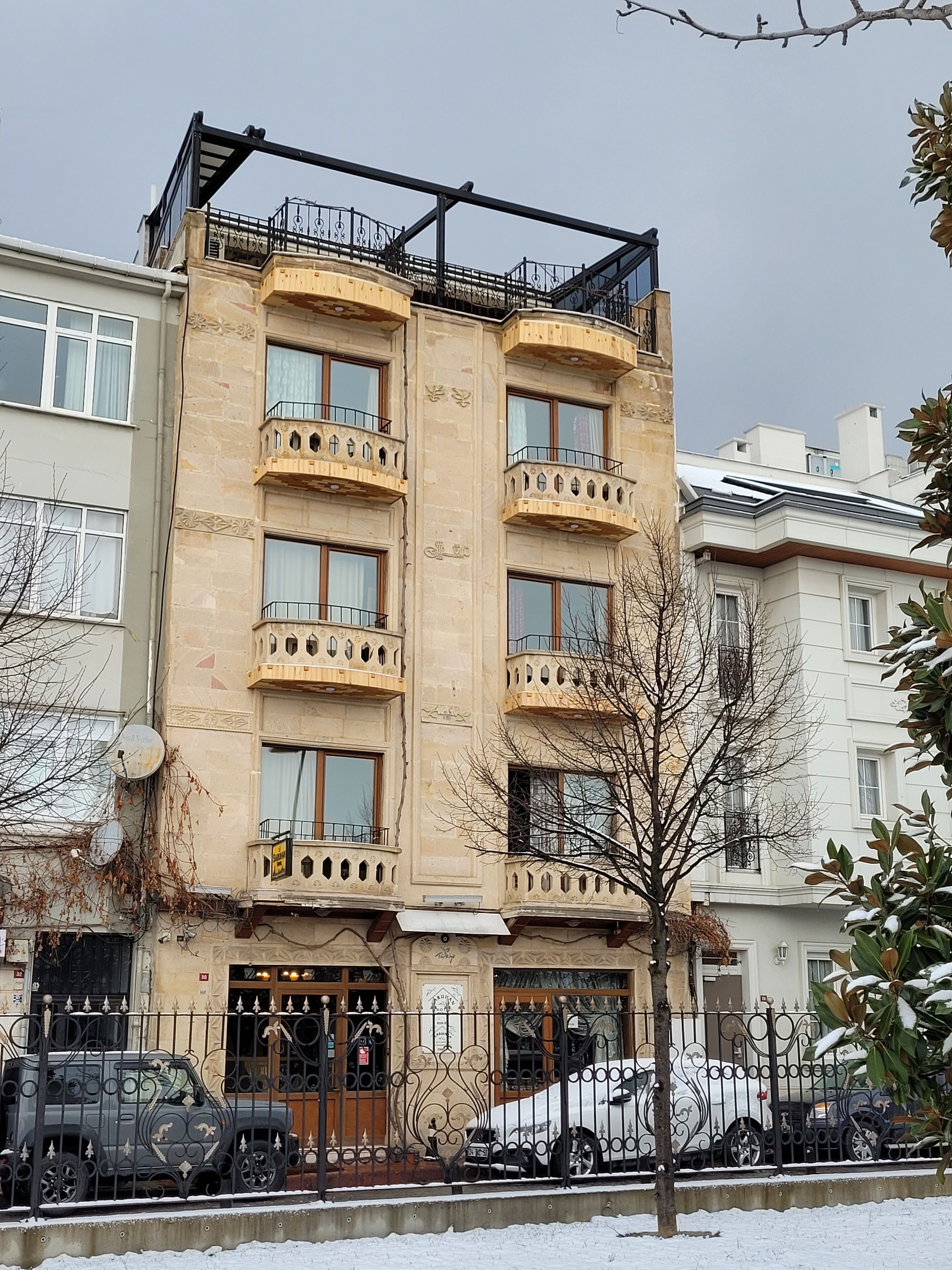 A multi-story building with balconies, a gated entrance, and parked cars.