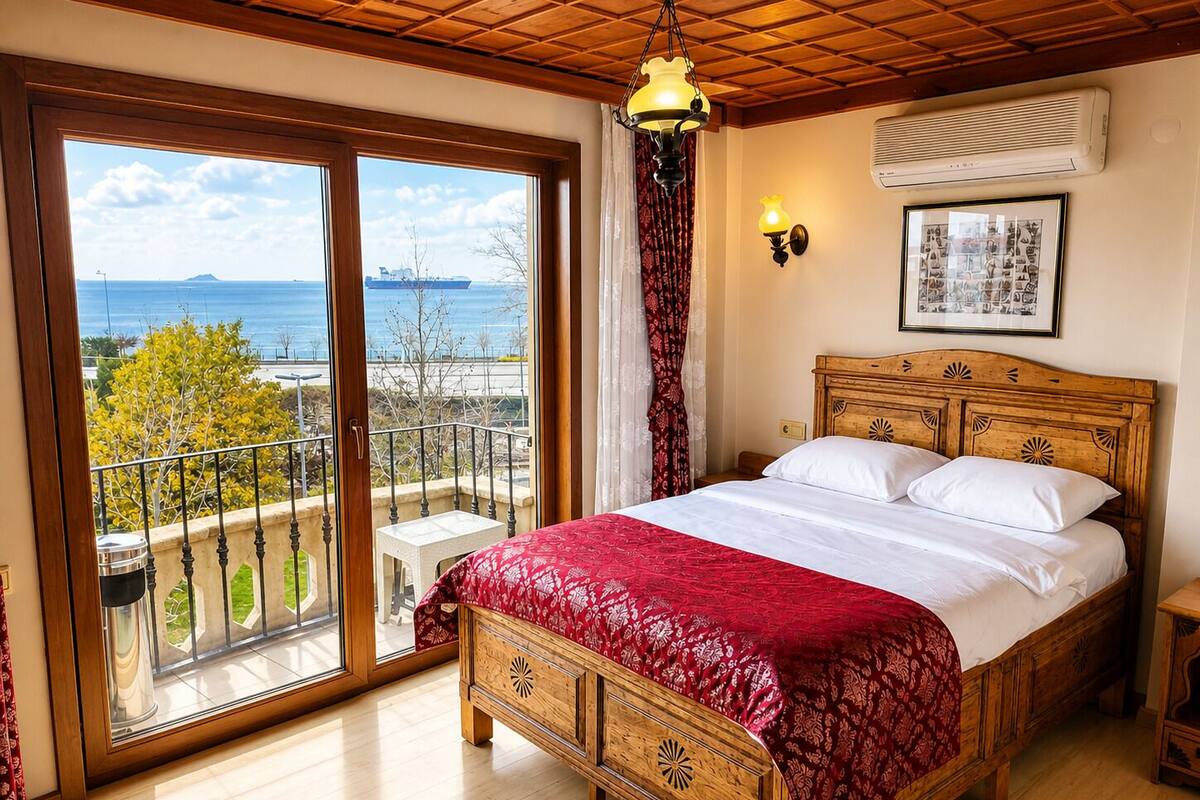 A bedroom with a wooden bed, a balcony with a view of the sea, and a ceiling fan.