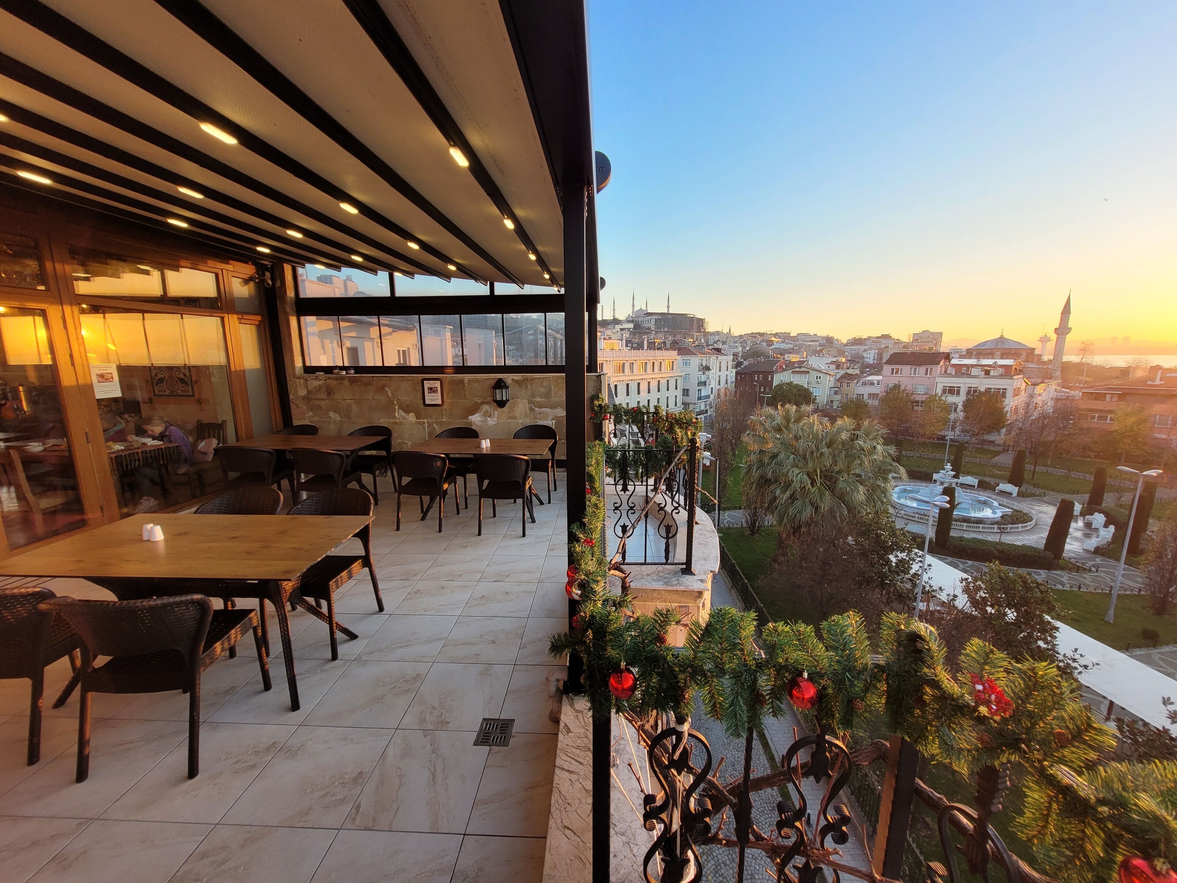 An outdoor seating area with tables and chairs, a view of the cityscape, and a decorative railing with greenery.