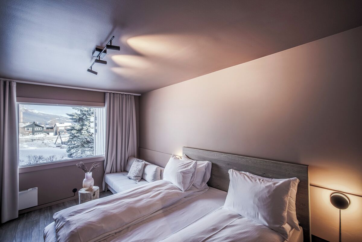 A hotel room with a bed, a bedside table, a lamp, and a window with a view of a snowy landscape.