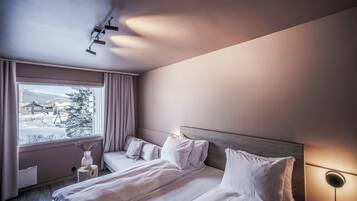 A hotel room with a bed, a bedside table, a lamp, and a window with a view of a snowy landscape.