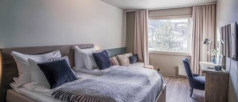 A modern hotel room with a large bed, a desk, and a chair.