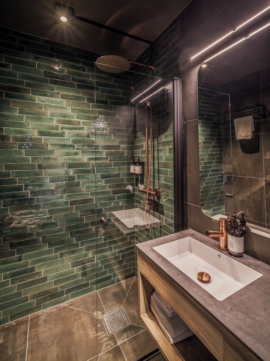 Un baño moderno con mosaicos verdes, dos lavamanos y un espejo grande.