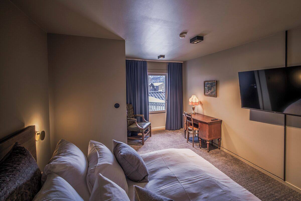 Ein Hotelzimmer mit Bett, Schreibtisch, Sessel, Fernseher und einem Fenster mit Vorhängen.