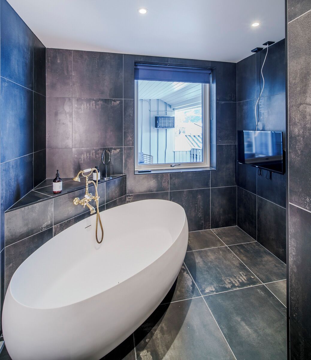 Un baño moderno con una bañera independiente, una ventana con vistas y un televisor de pared.