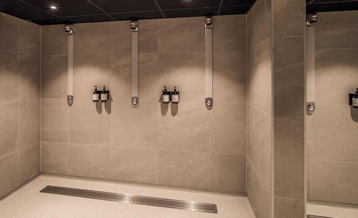 A restroom with four towel dispensers mounted on the wall, a floor drain, and a tiled ceiling.