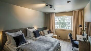 A modern hotel room with a large bed, a desk, and a window with curtains.