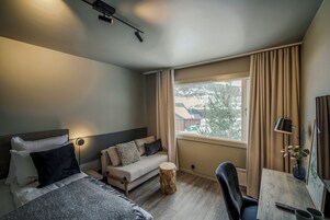 Una habitación de hotel moderna con cama, sofá, una mesita y una ventana con cortinas.