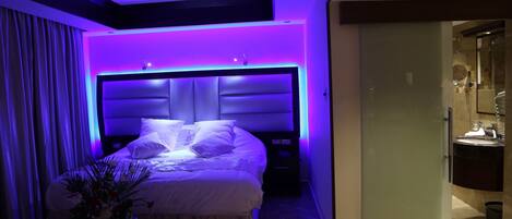 A modern bedroom with a large bed, a nightstand, and a bathroom visible through an open door.