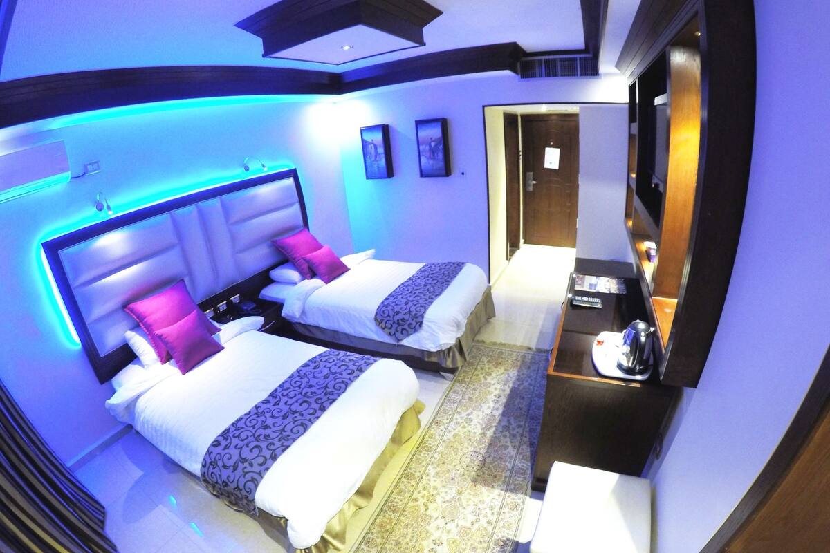 A modern hotel room with two beds, a small sitting area, and a television.