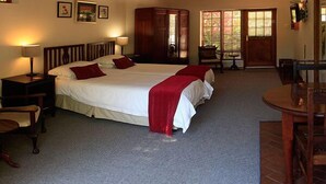A spacious bedroom with a large bed, a wooden wardrobe, a desk, and a chair. - Mongoose Manor (Gqeberha (Port Elizabeth))