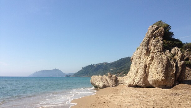 A beach with clear blue water, sandy shore, and rocky cliffs. - The Pink Palace (Corfu)