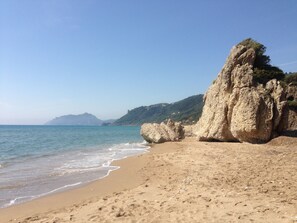 A beach with clear blue water, sandy shore, and rocky cliffs. - The Pink Palace (Corfu)