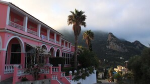 A pink building with balconies and a palm tree in front. - The Pink Palace (Corfu)