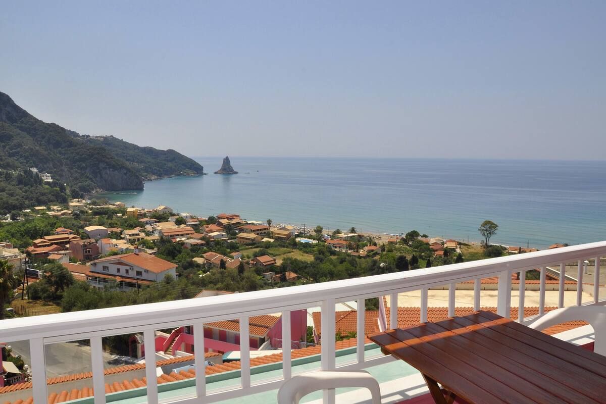 A balcony with a view of a coastal town, featuring terraced houses and a clear blue sea.