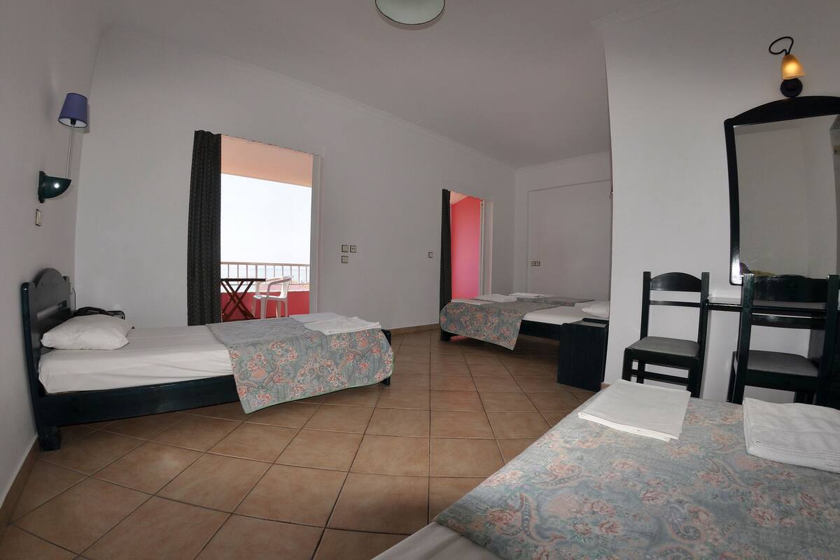 A hotel room with two beds, a desk, a chair, a mirror, and a balcony with a red railing.