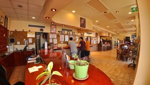 A reception area with a wooden reception desk, a green plant, and several people interacting. - The Pink Palace (Corfu)