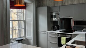 A modern kitchen with stainless steel appliances, a large island with bottles, and pendant lighting.