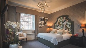 A bedroom with a large bed, a chandelier, a view of the city through the window, and a geometric wall design.