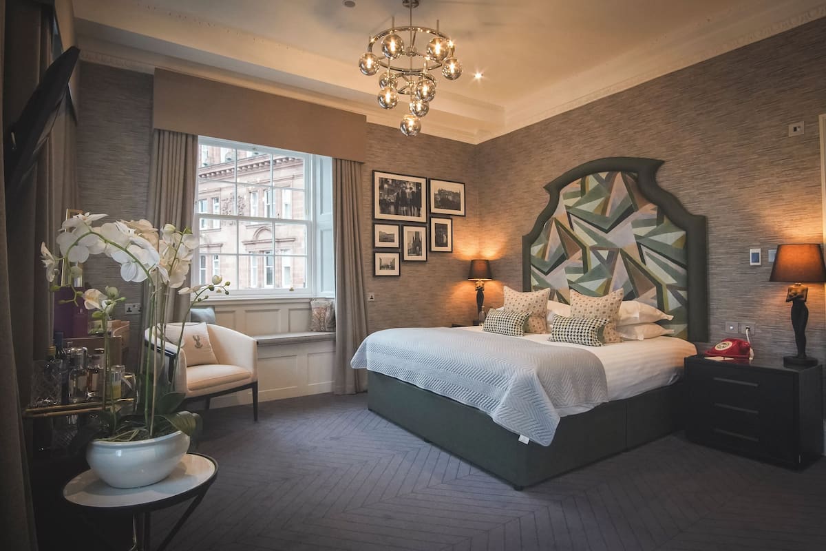 A bedroom with a large bed, a chandelier, a view of the city through the window, and a geometric wall design.