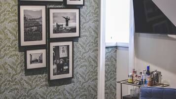 Um quarto com piso em padrão herringbone, um sofá azul com almofada estampada, e uma parede decorada com fotografias em preto e branco emolduradas.