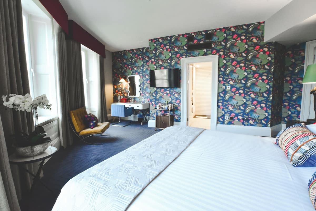 A hotel room with a large bed, a desk, a chair, a TV, and a bathroom door.