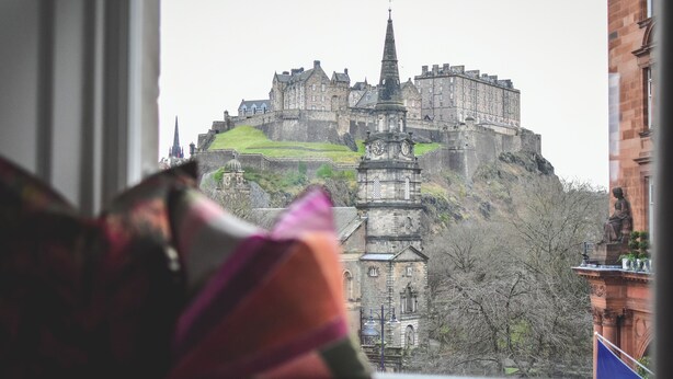 A view of a historic castle from a window, with a statue in the foreground.