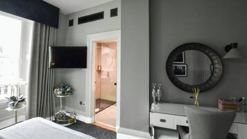 Ein Hotelzimmer mit einem Bett, einem Schminktisch mit Spiegel, einem an der Wand montierten Fernseher und einer Tür zu einem Badezimmer.